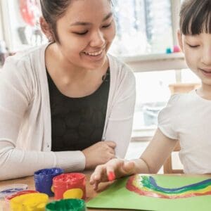 Young girl paints rainbow with teacher.