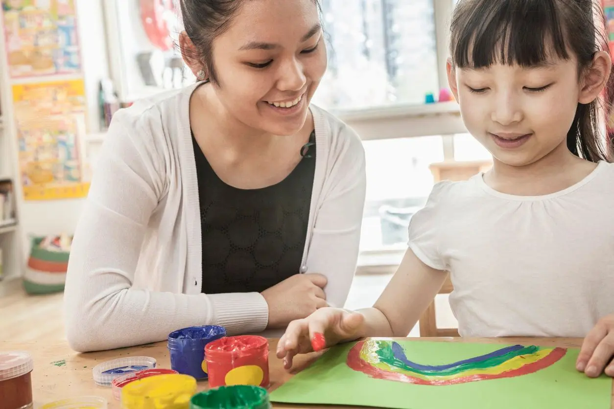 Young girl paints rainbow with teacher.