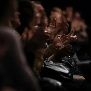 Audience clapping in a dark room.