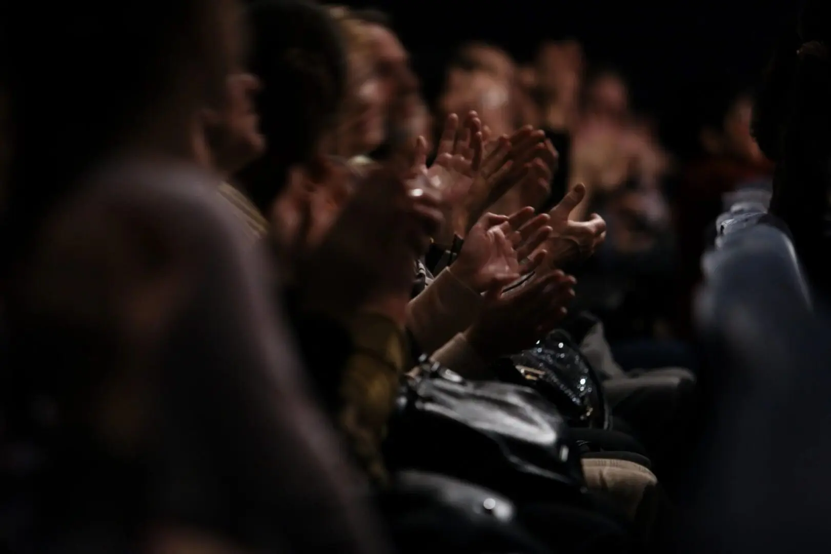 Audience clapping in a dark room.